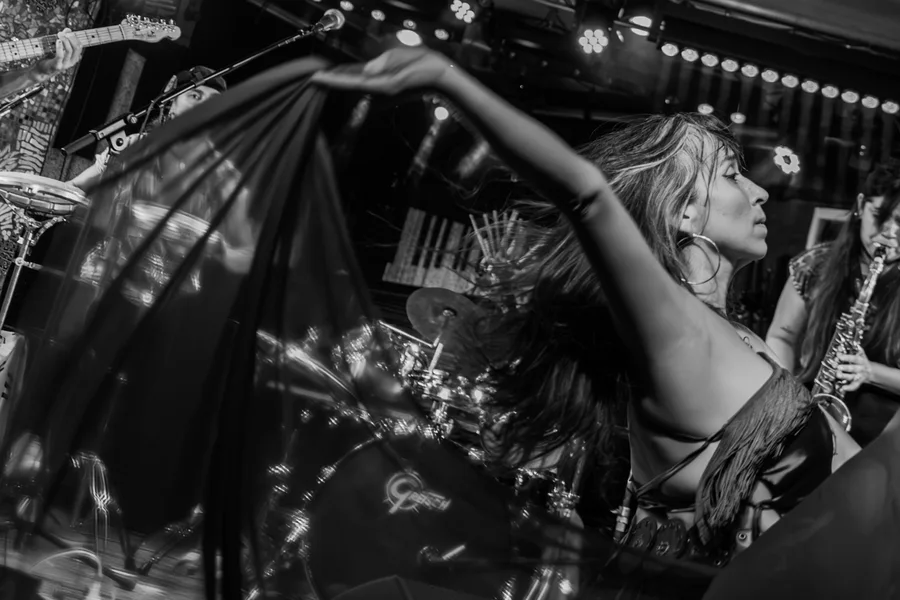 A dancer sweeps flowing fabric across the frame in front of a live band.