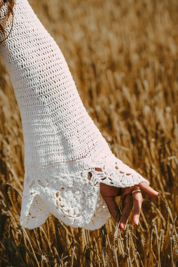 A hand brushes wheat beneath a white crochet sleeve.