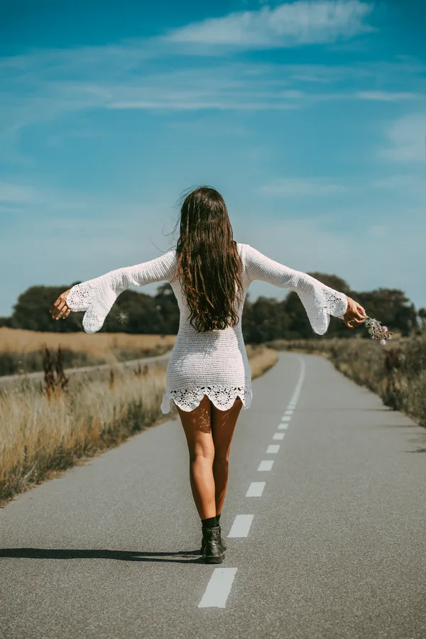 A woman walks away along a country road with her arms outstretched.