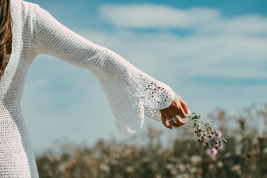 An outstretched arm holds a small bunch of wildflowers against the sky.