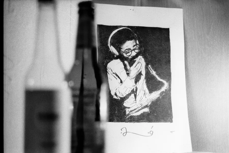 A saxophonist illustration beside a blurred bottle in grainy black and white.